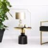 Runt svart sidobord med gulddetaljer och bordslampa i glas och beige.