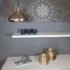 Guldig metallampel hängande i modern inredning med dekorativa vaser och bok.