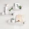 Tre vita flytande vägghyllor med dekorationer och konstverk.