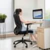 Kvinna använder ergonomisk kontorsstol framför dator med graf på skärm.