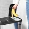 Person slänger banan i svart stålpedalbehållare för avfallshantering.