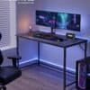 Litet svart metallramsskrivbord med dualmonitor setup och gamingutrustning.
