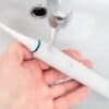Elektrisk tandborste i hand med vattenkran i bakgrunden.