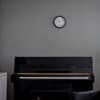 Svart piano under väggklocka i ett minimalistiskt vardagsrum.