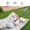 Avslappnad kvinna i hammock i trädgården med bok och kudde.