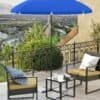 Blå parasol på terrass med utemöbler och utsikt över staden.