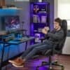Ung man i gamingstol med hörlurar, leende och avslappnad i hemkontor.