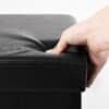 Närbild av svart läderförvaringspuff med hand som trycker på hörnet.