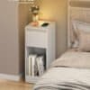Vit nattduksbord med eluttag, LED-lampa och böcker.