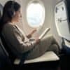 Kvinna med hörlurar läser bok på flygplanssäte.