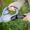 Person använder batteridriven bladblåsare i trädgården för löv och damm.